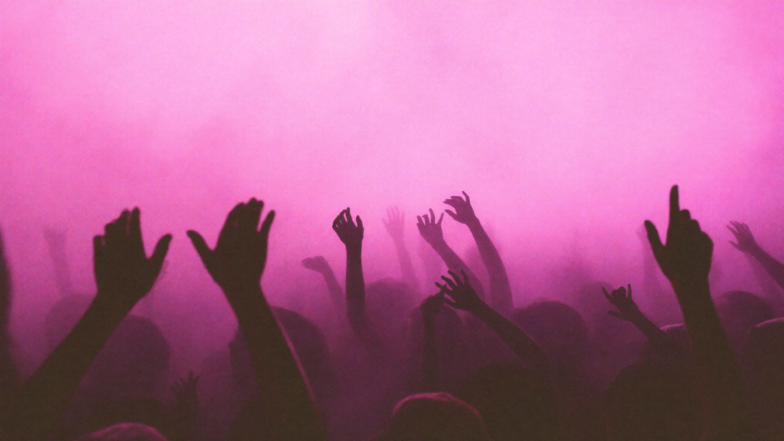 Gente con las manos en alto bajo luz rosa en un concierto: la noche antes de la resaca
